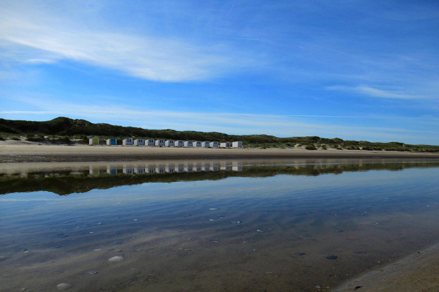 De strandhuisjes weerspiegelen in het achtergebleven water op het strand - Foto: ©Louis Fraanje