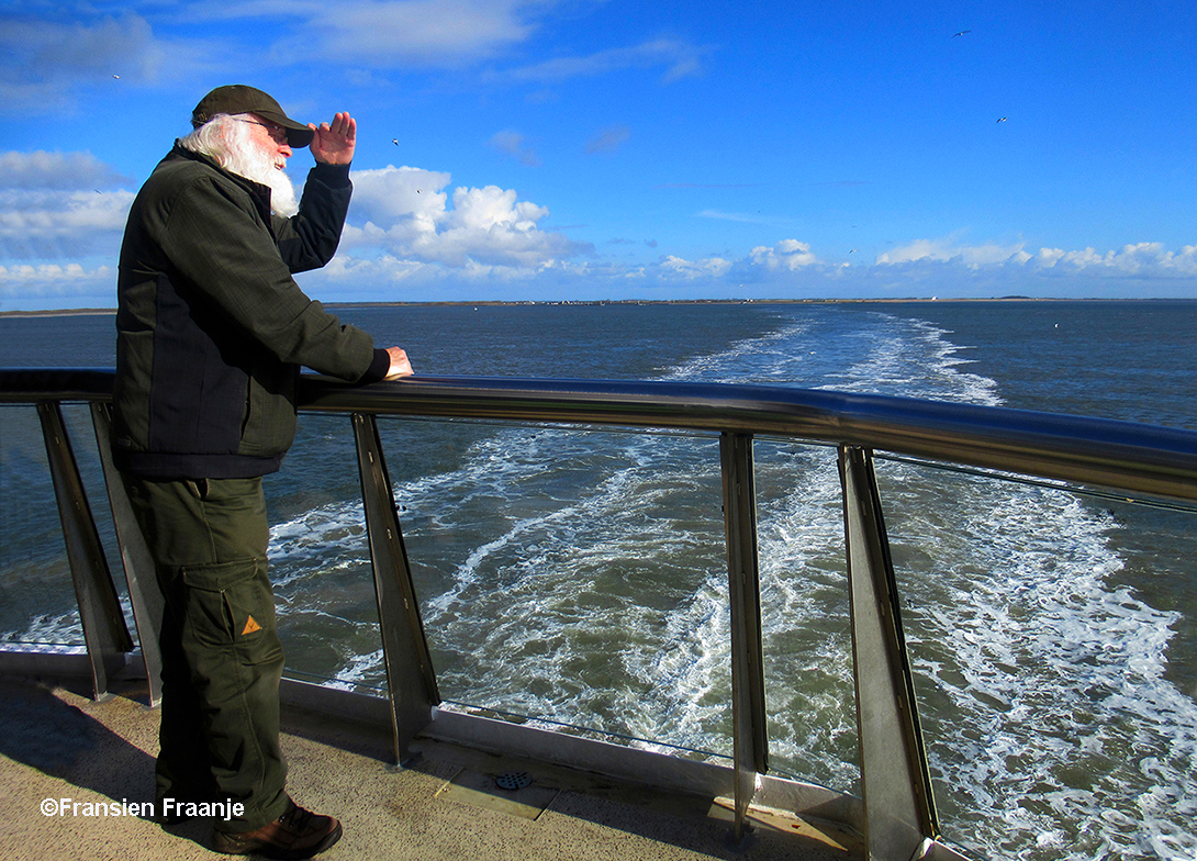 Louis staande op de achtersteven van de veerboot, turend over het water naar de horizon – Foto: ©Fransien Fraanje