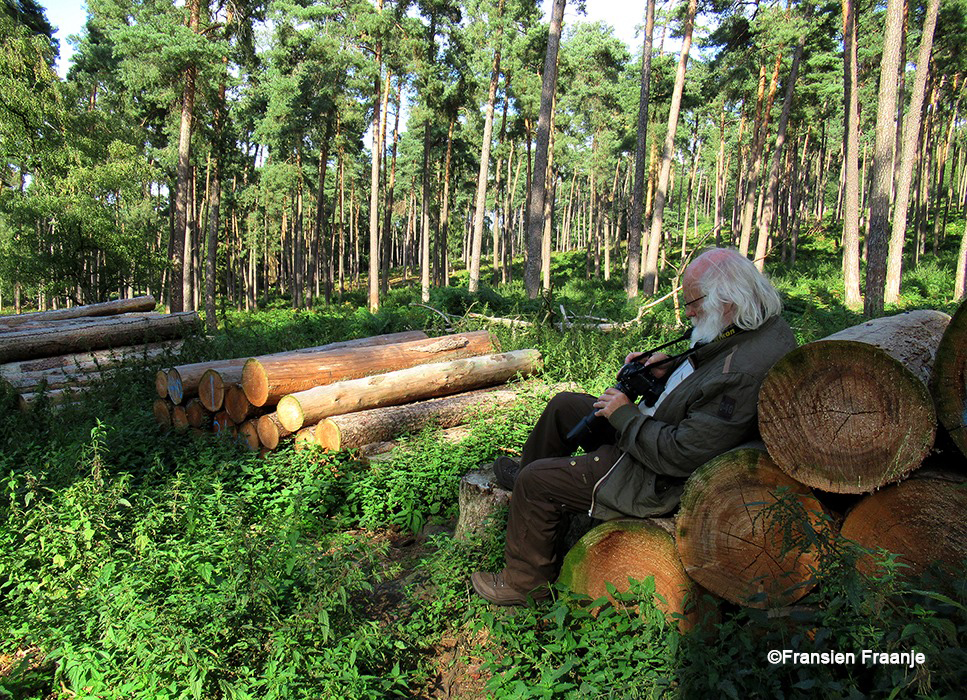 Daar zit Louis op een stapel boomstammen, net als vroeger toen hij in het bos werkte, maar nu bekijkt hij zijn plaatjes op de camera - Foto:© Fransien Fraanje