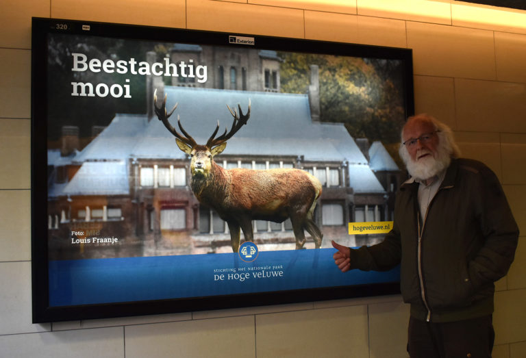 Een trotse fotograaf bij zijn winnende foto als verlichte ‘poster’ op het station Apeldoorn – Foto: ©Fransien Fraanje